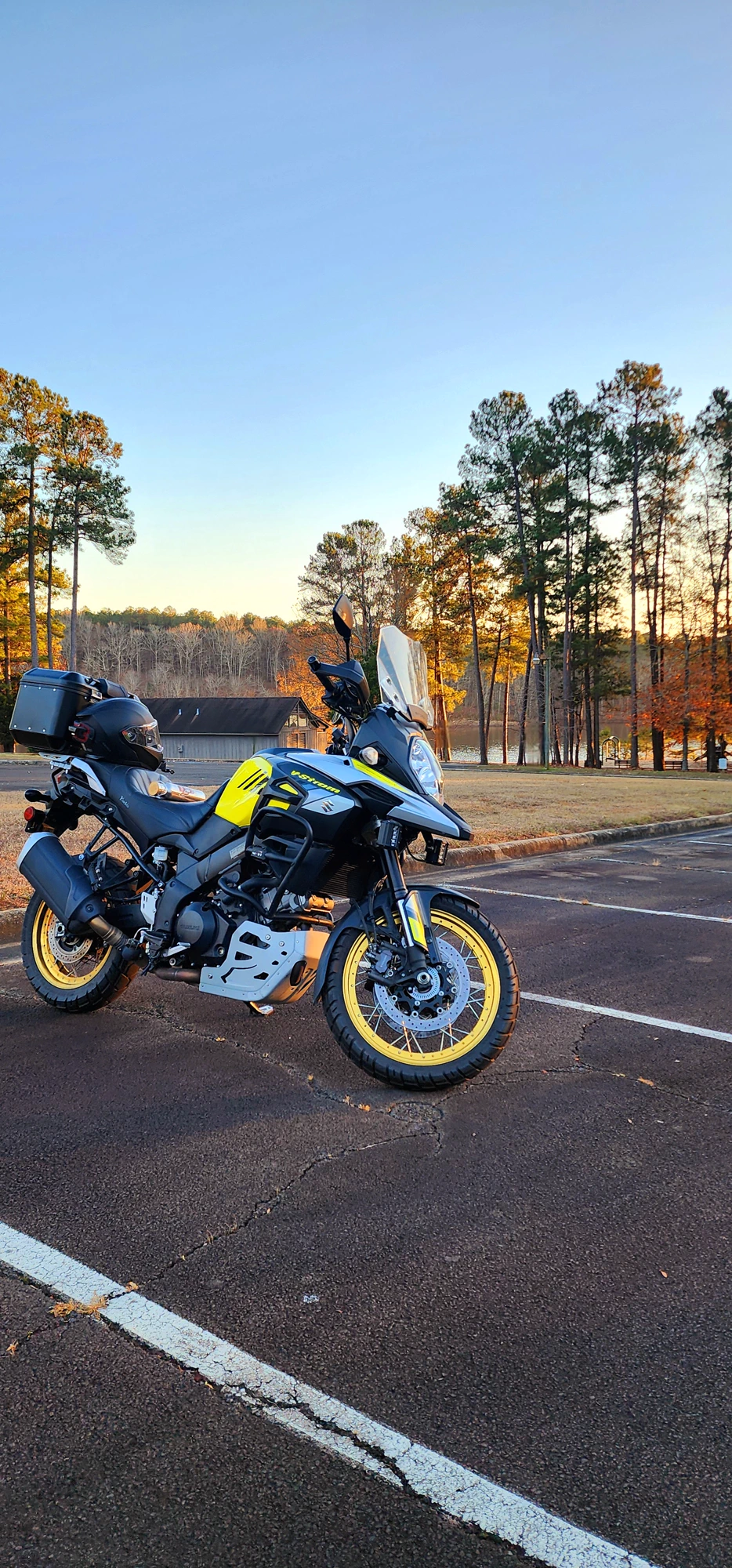 A Suzuki V-Strom motorcycle parked beside a lake in late-afternoon light.